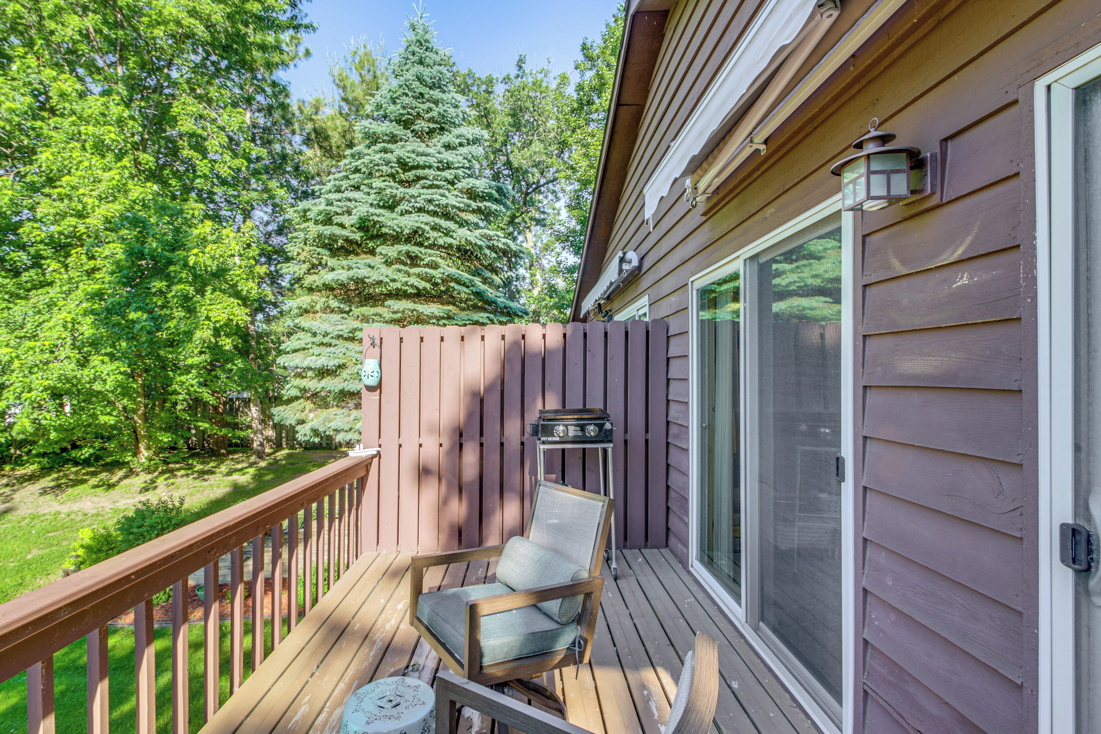 A wooden deck with a chair and a small table, a sliding glass door, and a wooden fence.
