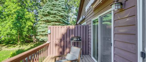 A wooden deck with a chair and a small table, a sliding glass door, and a wooden fence.
