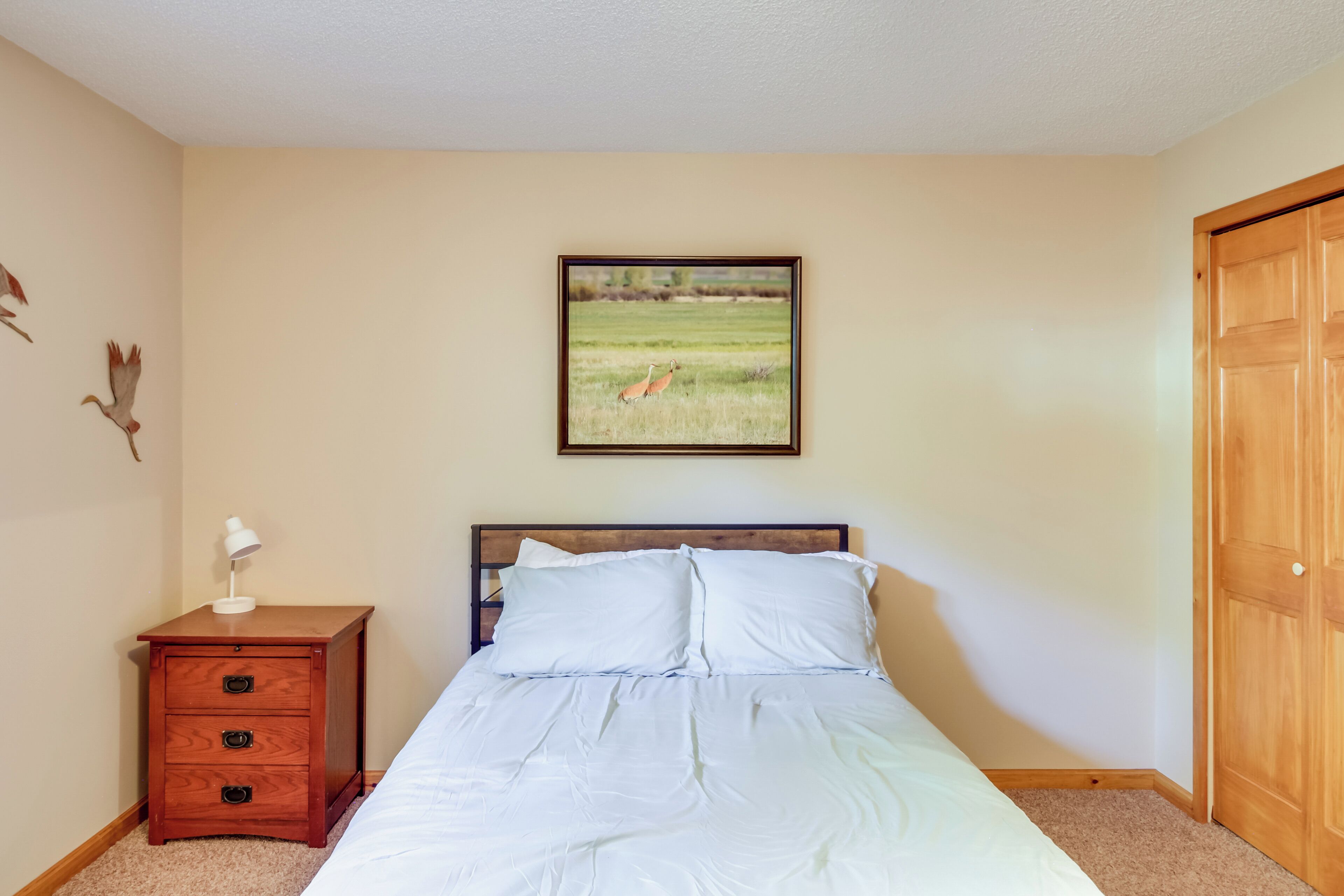 Una camera da letto con un letto, un comodino con una lampada, una porta in legno e un quadro appeso al muro.