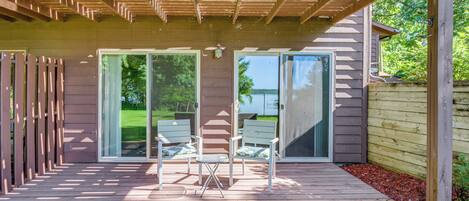 A covered patio area with a wooden deck, two folding chairs, and a table.
