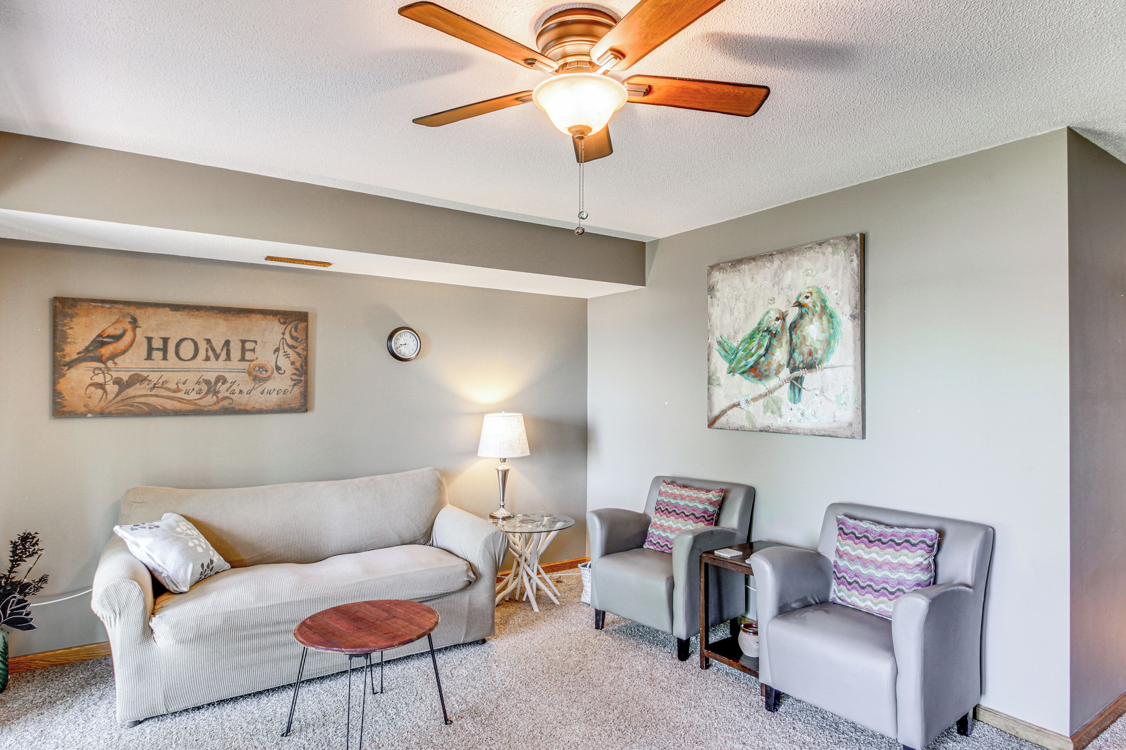 A living room with a ceiling fan, a sofa, two armchairs, a coffee table, and artwork on the walls.