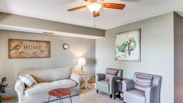 A living room with a ceiling fan, a sofa, two armchairs, a coffee table, and artwork on the walls.