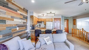 A modern living room with a gray sofa, a wooden accent wall, and a kitchen in the background. - Beach & Lake Access: Brainerd Townhome (Brainerd)