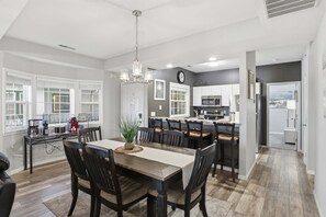 Una cocina moderna con armarios blancos, una isla central y un comedor con mesa y sillas de madera.