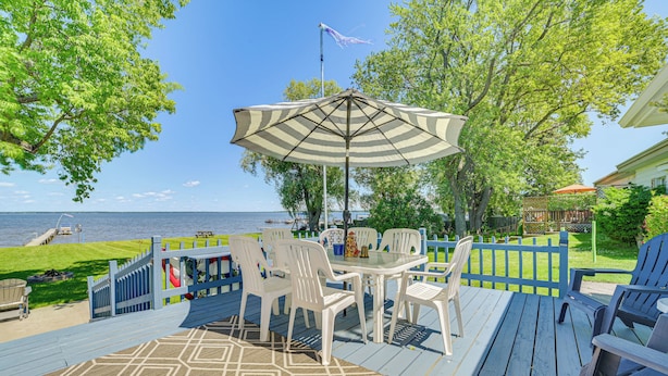 A deck with a table and chairs, a patterned rug, and a view of the water. - Private Dock & Fire Pit: Houghton Lake Home! (Houghton Lake)