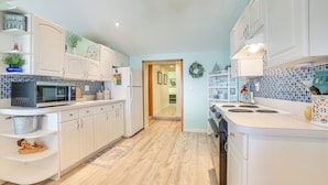 A modern kitchen with white cabinets, a microwave, a stove, and a sink. There is a wooden floor and a blue-tiled backsplash. - Private Dock & Fire Pit: Houghton Lake Home! (Houghton Lake)