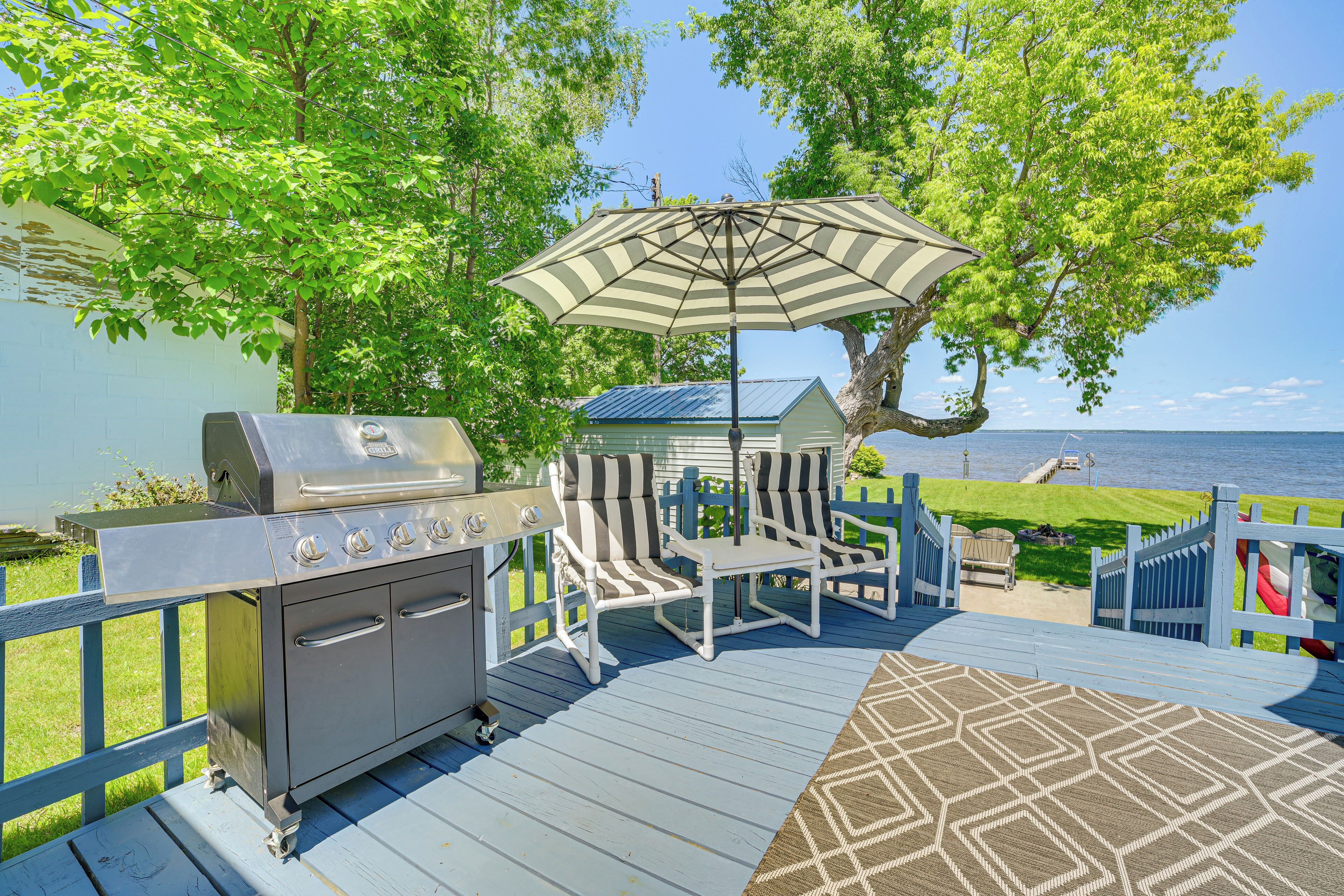 A deck with a grill, striped chairs, and an umbrella.