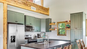 A modern kitchen with green cabinets, stainless steel appliances, and a central island with bar stools.