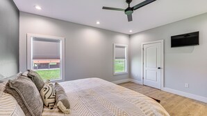 A bedroom with a bed, pillows, a ceiling fan, and two windows.
