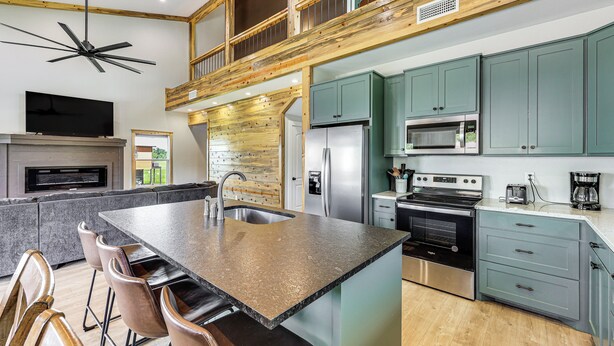 A modern kitchen with a large island, stainless steel appliances, and a TV mounted above the island.