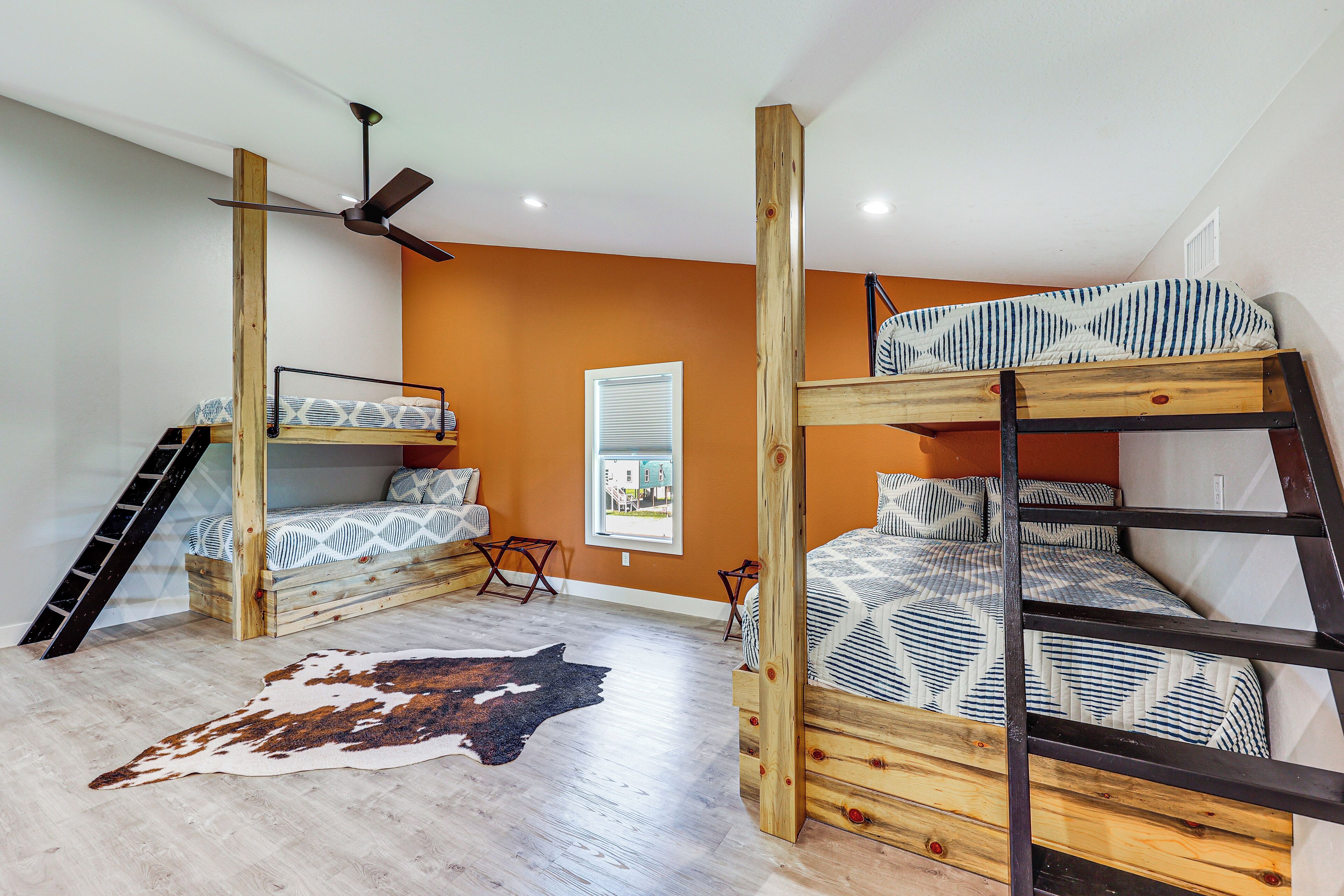 Une chambre avec deux lits superposés, un ventilateur de plafond, une fenêtre avec des stores et un tapis en peau de vache.