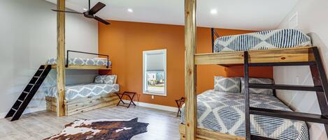 Une chambre avec deux lits superposés, un ventilateur de plafond, une fenêtre avec des stores et un tapis en peau de vache.