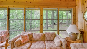 A cabin interior with a large window, a sofa, a chair, and a lamp. - Sullivan Lake Cabin w/ Pierz & Hillman Access! (Hillman)