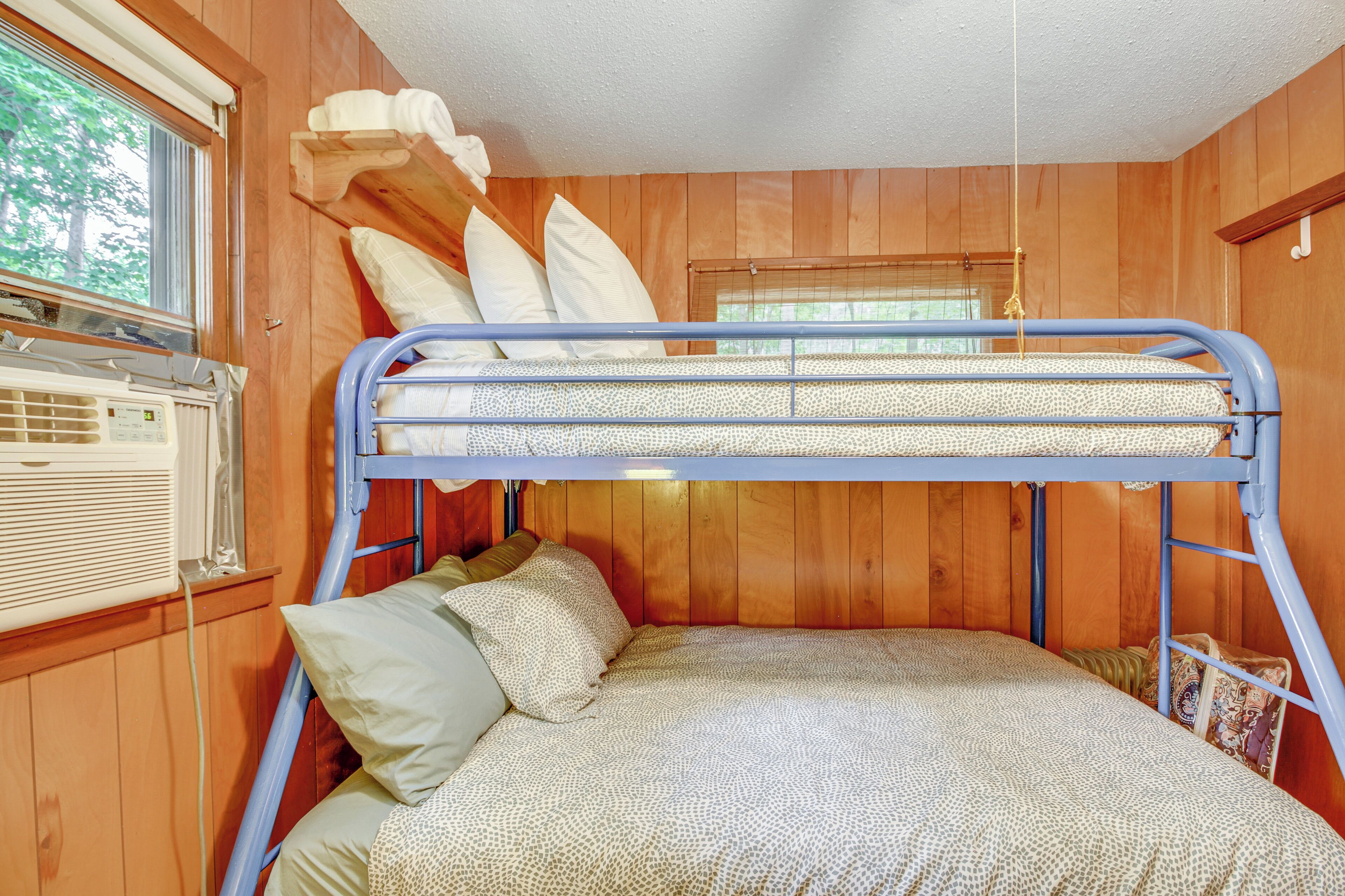 A bunk bed with a patterned bedspread, pillows, and a window with blinds.