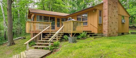 A cabin with a wooden deck, a chimney, and a staircase leading to the entrance.