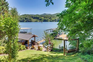 A lakeside property with a wooden deck, outdoor seating, and a swing chair.
