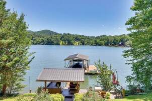 A lakeside cabin with a dock, surrounded by lush greenery and a clear view of the lake.