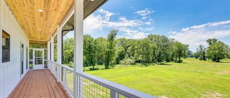 A covered wooden deck with a view of a green field and trees.