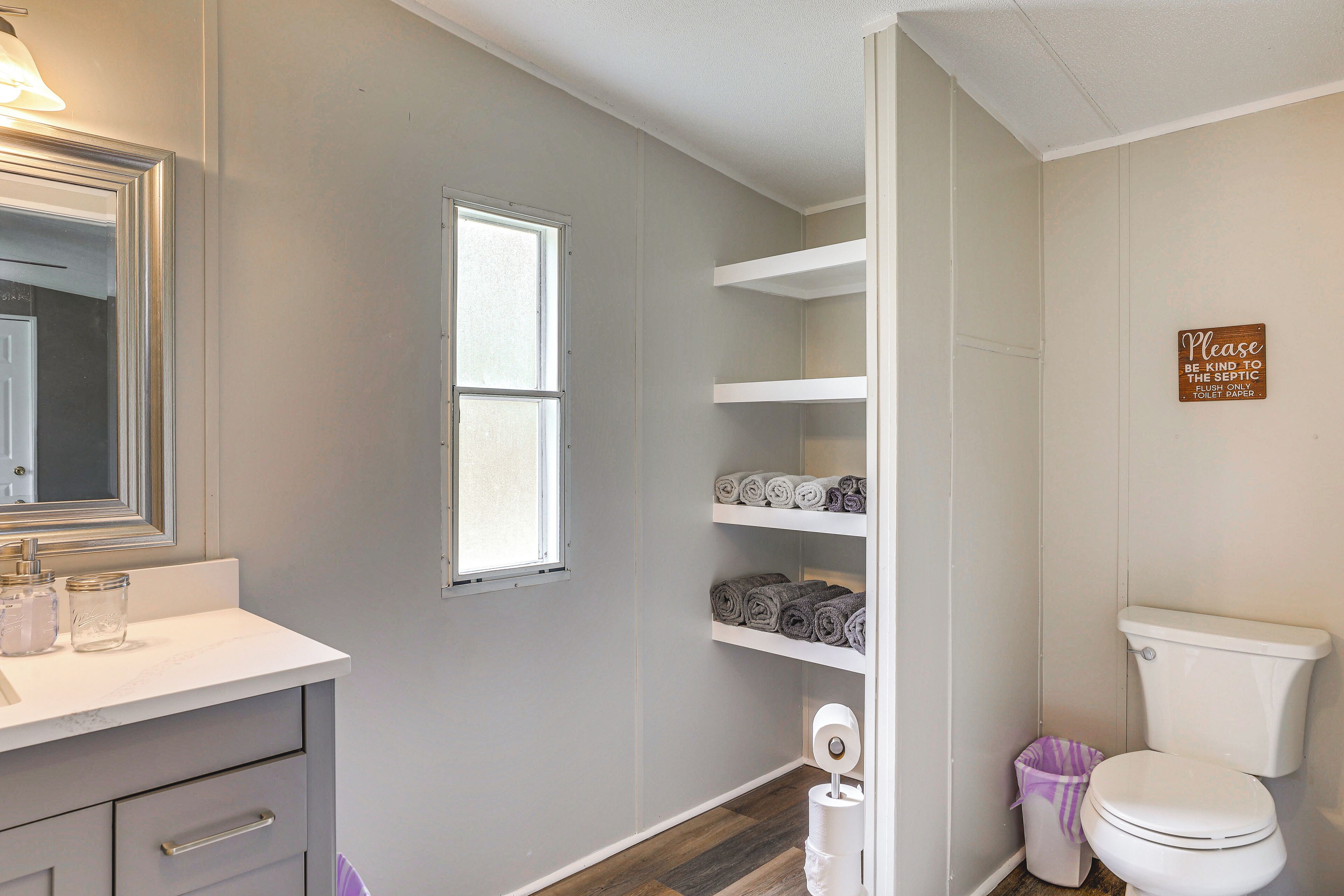 A bathroom with a toilet, a shelf with towels, a mirror, and a sign instructing to flush only toilet paper.