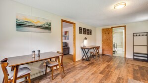 Une pièce avec une table à manger en bois, des chaises, un tableau et une porte en bois donnant sur une autre pièce.