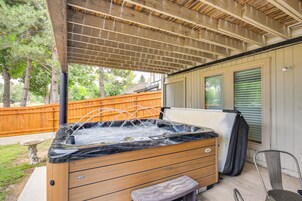 Un jacuzzi bajo un porche cubierto, con una terraza de madera, un bebedero de piedra para pájaros y un banco de madera.