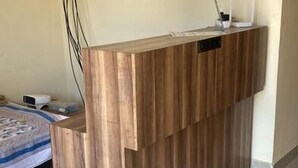 A reception desk with a wooden finish, a framed certificate on the wall, and a bed with a patterned bedspread in the background. - Hotel Padmawati By GRB Stays (Abu Road)