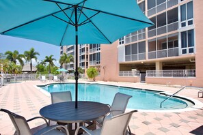 A pool area with a round table and chairs, surrounded by a tiled deck. - 🌴Great Water Views, Fabulous Location-Palm Harbor #403🌴 (Fort Myers Beach)
