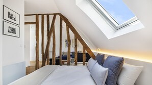 A bedroom with a sloped ceiling, wooden beams, a skylight, a bed with pillows, and a desk with a chair. - Miel, 1BR/1BA, 3 people (París)