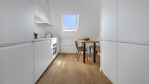 A compact kitchen with white cabinets, a wooden floor, a small table with a chair, and a skylight. - Miel, 1BR/1BA, 3 people (París)