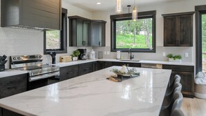 A modern kitchen with dark cabinetry, a large island, stainless steel appliances, and pendant lighting.