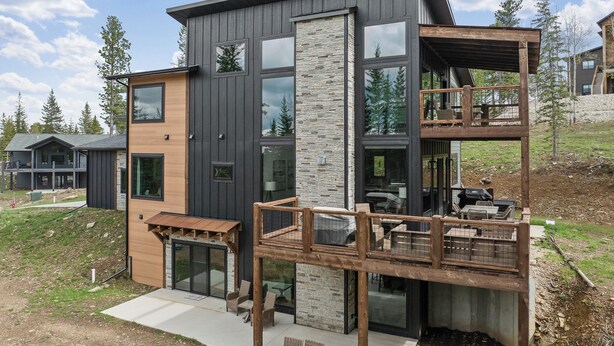 A modern two-story house with a balcony, large windows, and a stone facade.