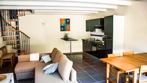 A modern living room with a sofa, a dining table, and a kitchen area with cabinets and a stove. - La Cigalière Gite Bleu Azur  (ELNE)