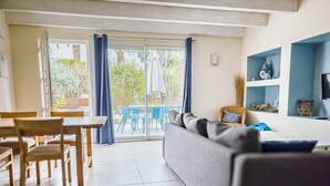 A spacious living area with a sliding glass door leading to a patio, a sofa, a dining table, and blue chairs. - La Cigalière Gite Bleu Azur  (ELNE)