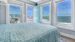 A bedroom with a large bed, two windows with ocean views, and a door leading to a balcony.