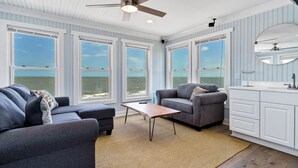A coastal living room with large windows, a ceiling fan, and a view of the ocean.