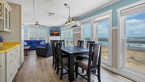 A spacious dining area with a large table and chairs, a blue sofa, and a view of the beach.