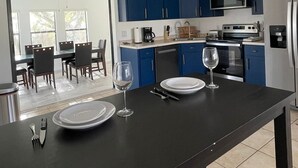 Une cuisine moderne avec des meubles bleus, un réfrigérateur en acier inoxydable et un coin repas comprenant une table et des chaises.