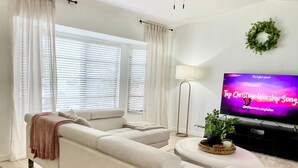 Un salon moderne avec un canapé d’angle, un ventilateur de plafond, un téléviseur diffusant les « meilleures chansons de louange chrétiennes » et une couronne décorative accrochée au mur.