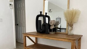 Une console en bois surmontée d’un miroir, un vase contenant des herbes des pampas séchées et un panier tressé.