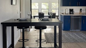 Une cuisine moderne avec un coin repas, comprenant une table en bois foncé accompagnée de deux tabourets, une machine à café et un lave-vaisselle.
