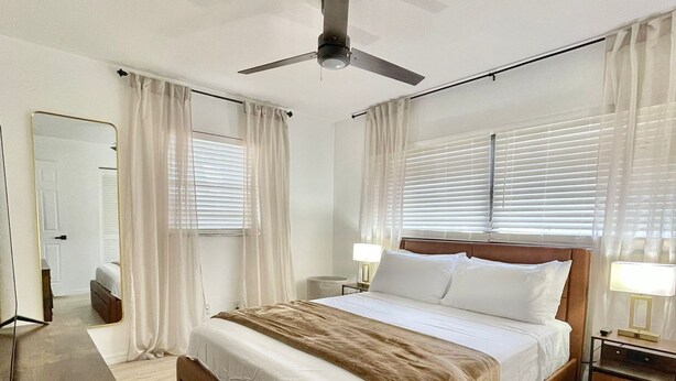 Une chambre spacieuse avec un grand lit, un ventilateur de plafond et une table de chevet avec une lampe.