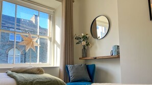 A bedroom with a large window, a star decoration, a mirror, a shelf with books, and a bed with pillows.