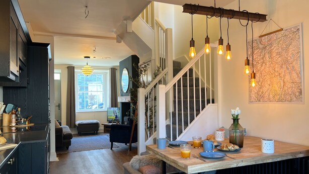A modern kitchen with dark cabinets, a wooden dining table, and a staircase leading to a loft bedroom.