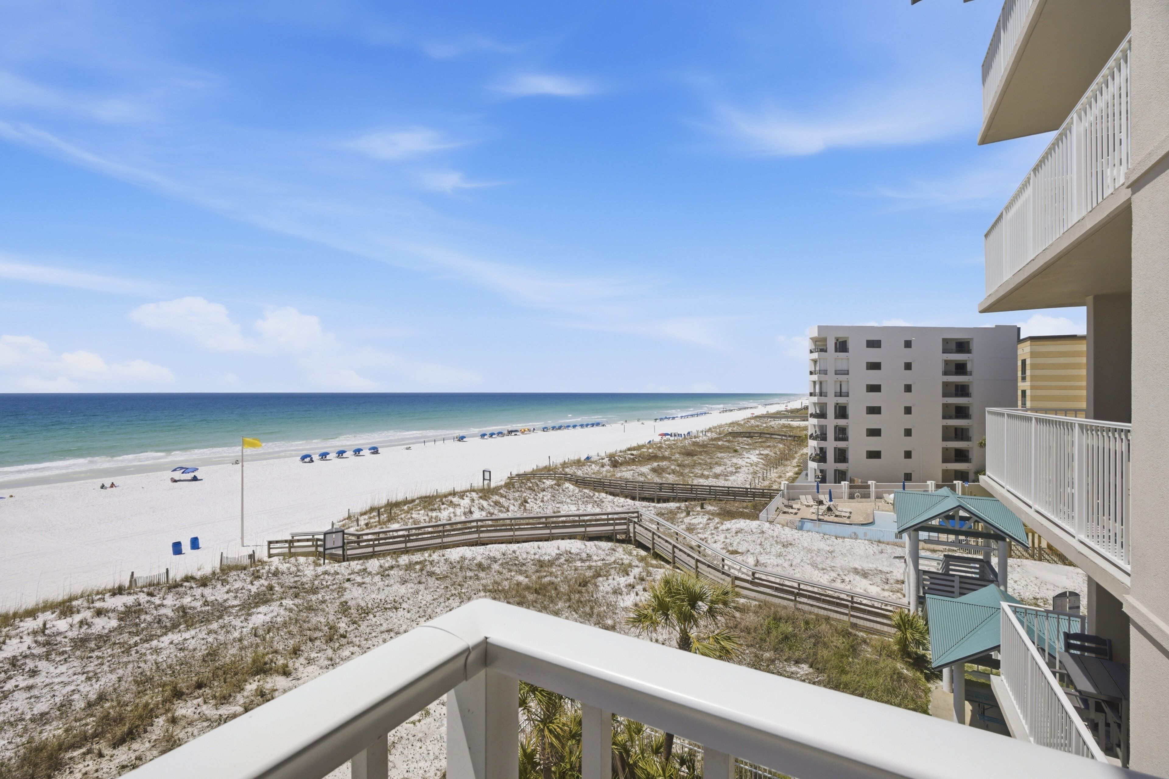 A beach view with a boardwalk, beach umbrellas, and a building with balconies.