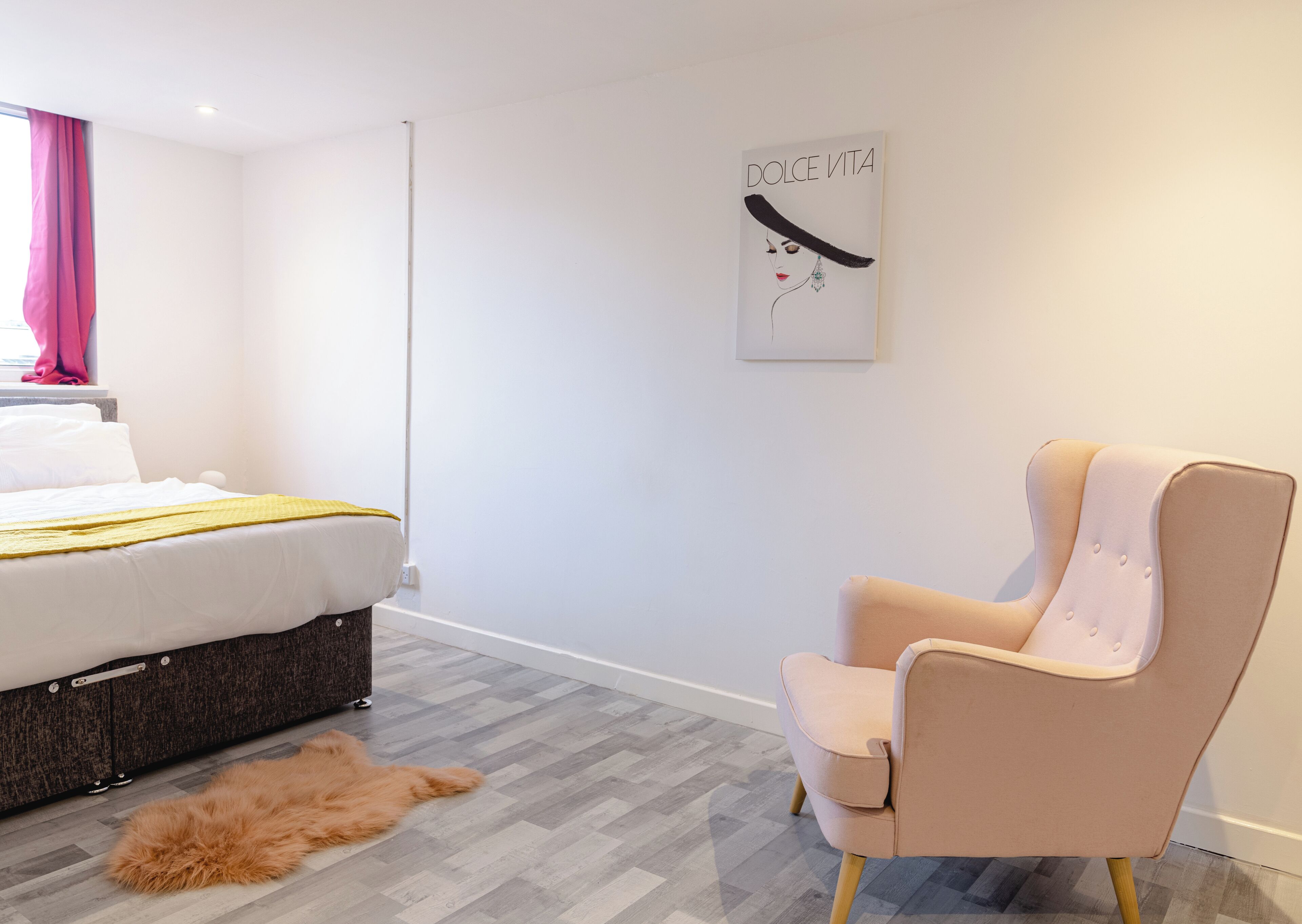 A modern bedroom with a bed, a chair, a rug, and a wall art piece.