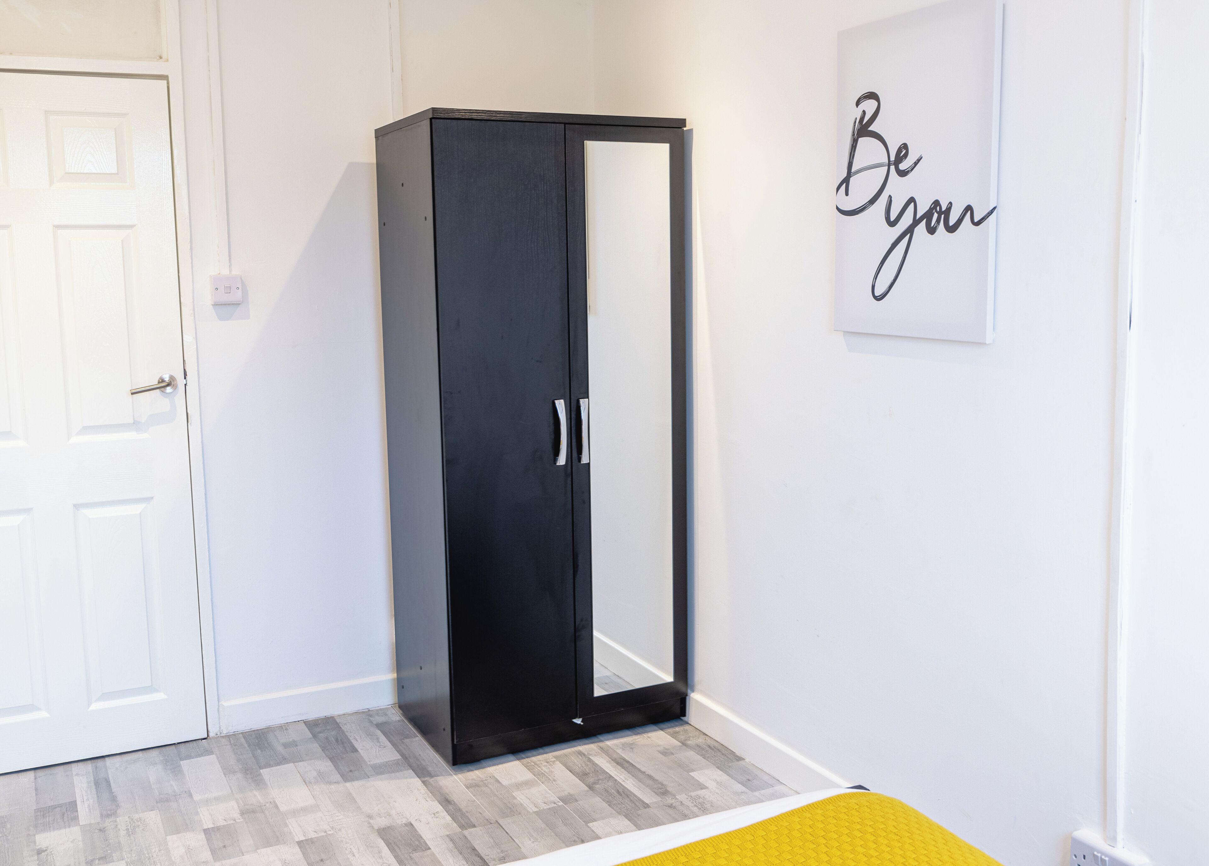 A room with a black wardrobe, a white door, and a wall with a 'Be your best' motivational quote.