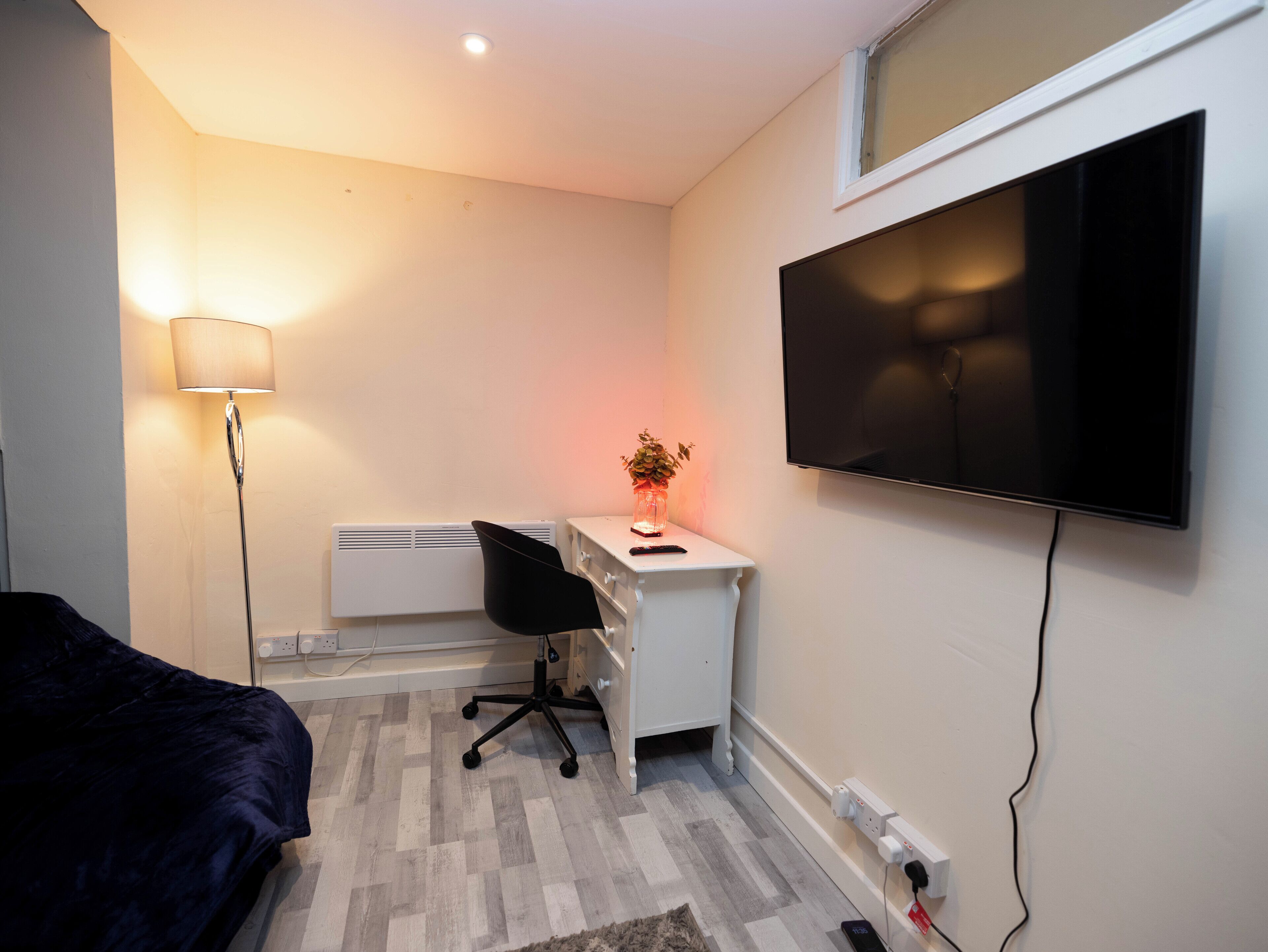 Un dormitorio con una cama, un escritorio con silla, un televisor y una lámpara.