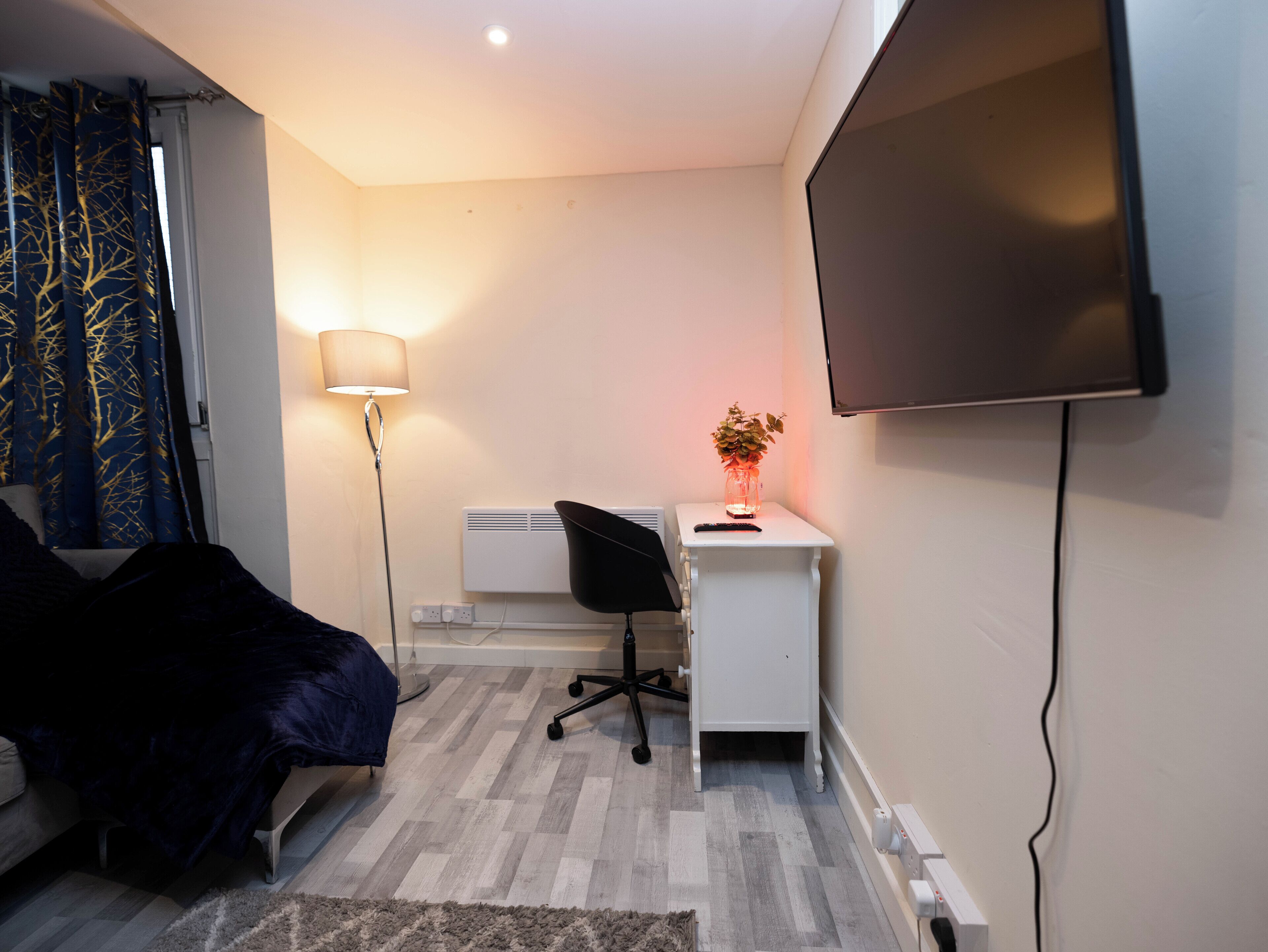 Une chambre à coucher avec un lit, un bureau et une chaise, une télévision et une lampe.