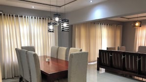 Un comedor con una mesa de madera y seis sillas tapizadas, un banco con respaldo de madera y una lámpara colgante moderna.