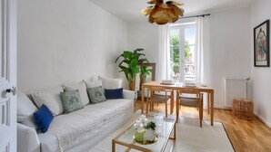A modern living room with a white sofa, a glass coffee table, and a dining area with a wooden table and chairs. - Flat in the town centre - 270m  l'Ecluse beach (Dinard)